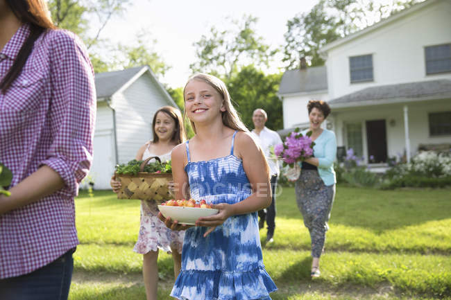 Parents et enfants marchant sur la pelouse portant des fleurs, des légumes frais et des fruits . — Photo de stock