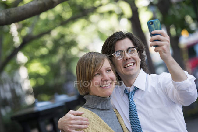 Mid adult man and woman posing for selfie with smartphone on street. — Stock Photo