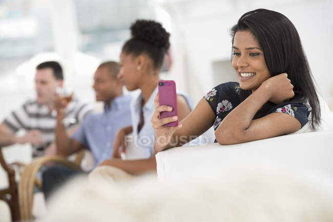 Woman using pink smartphone with people talking at party in background. — Stock Photo