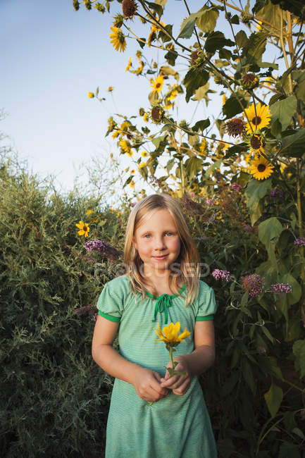 Vorpubertierendes Mädchen steht im Garten und hält Sonnenblumen in der Hand. — Stockfoto