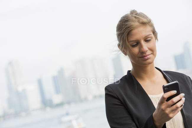 Young businesswoman in black jacket using smartphone in city downtown. — Stock Photo