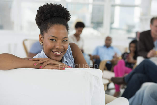 Frau lächelt und lehnt sich auf Sessel, im Hintergrund feiern Menschen. — Stockfoto