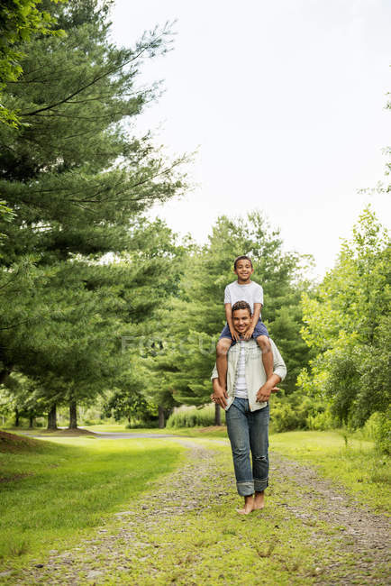 Pre-adolescent boy carrying brother on shoulders while walking on country path. — Stock Photo