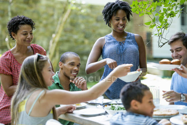 Friends and family gathering around dinner table in countryside garden. — Stock Photo