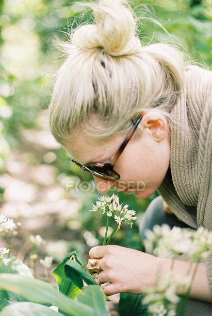 Frau mit Sonnenbrille lehnt sich zur Untersuchung von Blumen zurück. — Stockfoto