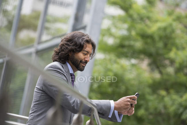 Seitenansicht eines Mannes im Anzug, der sich an ein Geländer lehnt und das Telefon benutzt. — Stockfoto