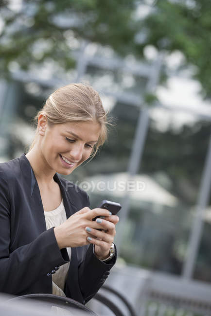 Young businesswoman in black jacket using smartphone in city. — Stock Photo