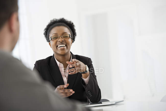 Жінка в чорному костюмі розмовляє з чоловіком за столом в офісі . — стокове фото
