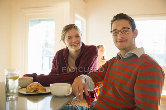Joven hombre y mujer sentado en el mostrador en la cafetería y mirando en la cámara . - foto de stock