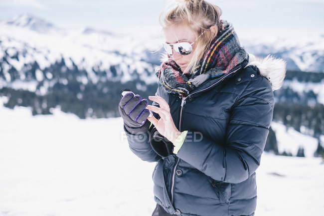 Mujer en ropa de invierno en la pista de esquí con smartphone . - foto de stock