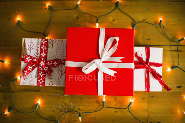 Gift boxes tied with red ribbons and fairy lights on wooden floor. — Stock Photo