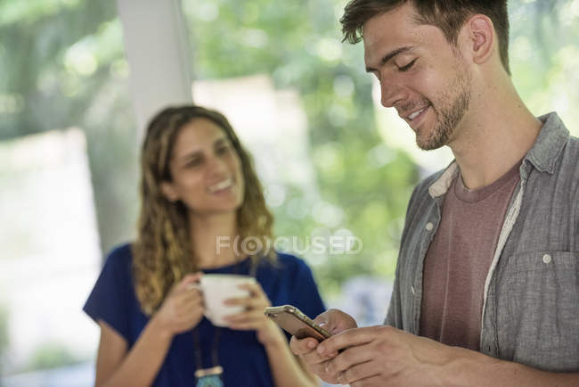 Homem verificando telefone e mulher segurando xícara de café . — Fotografia de Stock