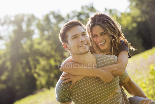 Man giving young woman piggyback in flower meadow in summer. — Stock Photo