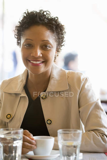 Жінка в бежевій куртці сидить за столом у кафе з чашкою кави . — стокове фото