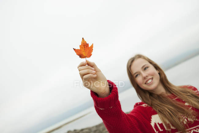 Teen girl in red knitted jumper holding maple leaf. — Stock Photo