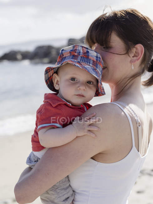 Mère tenant bébé fils sur la plage de sable . — Photo de stock