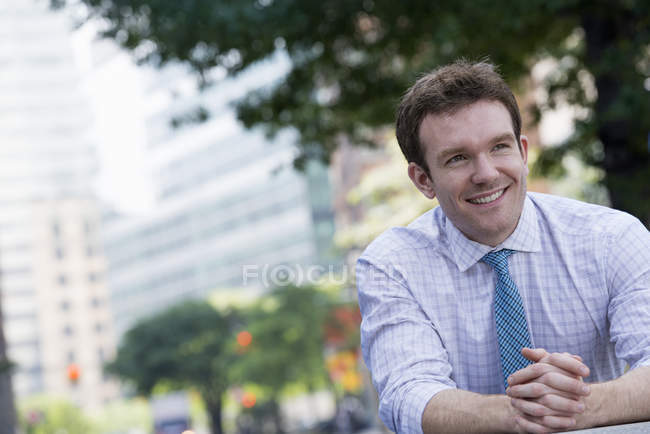 Businessman in shirt and tie with hands clasped leaning on railing in city. — Stock Photo