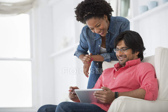 Людина на диван і стоїть жінка, дивлячись на цифровий планшетний в офісі. — стокове фото
