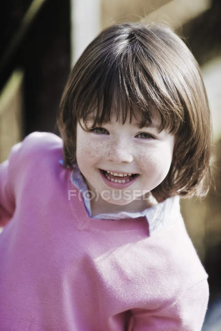 Junge im Grundschulalter mit braunen Haaren und Sommersprossen im rosa Pullover blickt in die Kamera. — Stockfoto