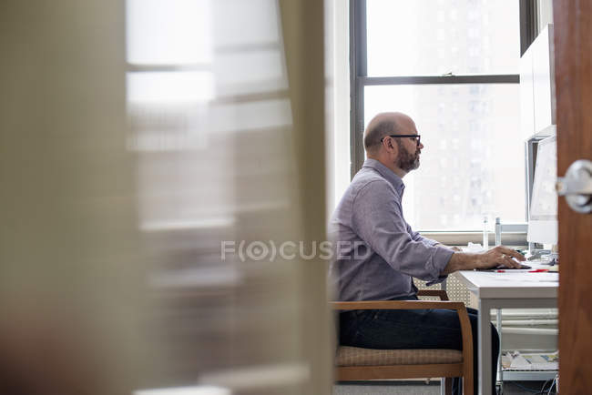 Side view of man sitting at desk and using computer in office. — Stock Photo
