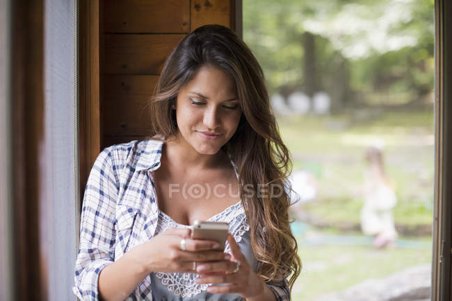 Mulher inclinada na parede com janela e olhando para o smartphone . — Fotografia de Stock