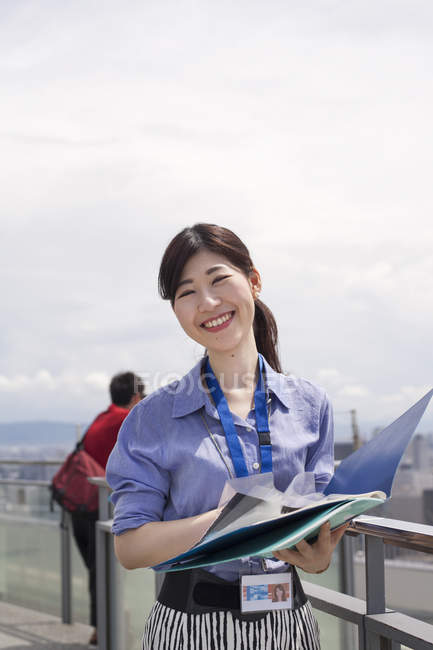 Smiling Japanese woman holding files on office building balcony. — Stock Photo