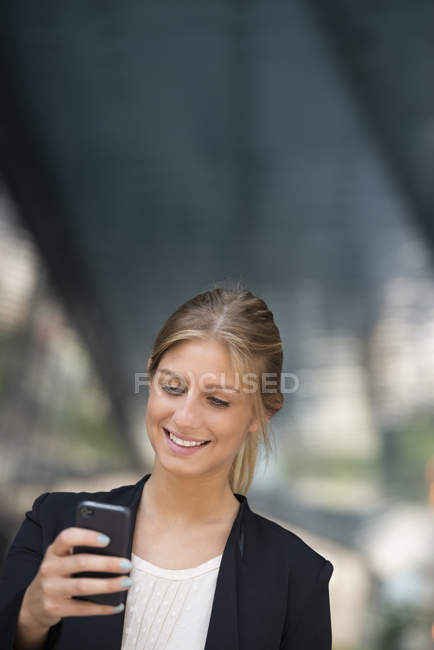 Jovem empresária de jaqueta preta usando smartphone na cidade . — Fotografia de Stock