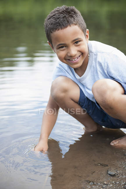 Menino da idade elementar pegando pedras na costa do lago . — Fotografia de Stock