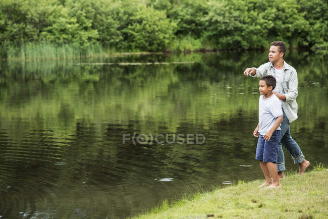 Dos hermanos tirando piedras en el agua en la orilla del lago en los bosques . - foto de stock