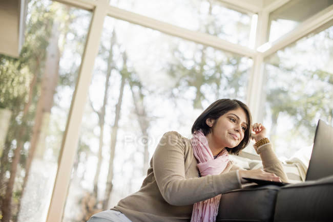 Mulher sentada no chão na frente do sofá e usando laptop . — Fotografia de Stock