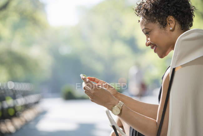 Жінка сидить у кріслі в міському парку і використовує смартфон . — стокове фото