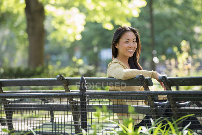Взрослая женщина, сидящая в городском парке на скамейке под солнцем . — стоковое фото