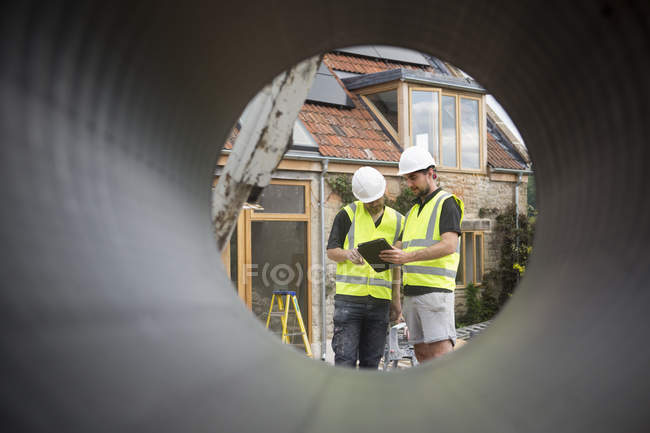 Dos trabajadores de la construcción en el sitio de construcción, vista a través de tubería redonda . - foto de stock