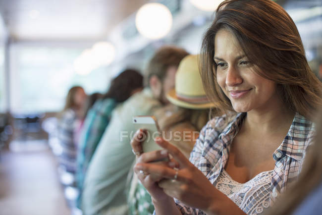Donna che guarda smartphone con fila di clienti in diner cafè . — Foto stock