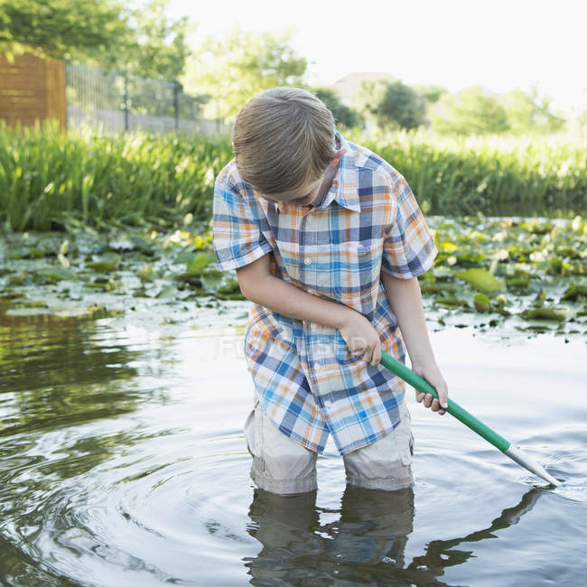 Menino da idade elementar em pé na água e usando rede de escavar no campo . — Fotografia de Stock