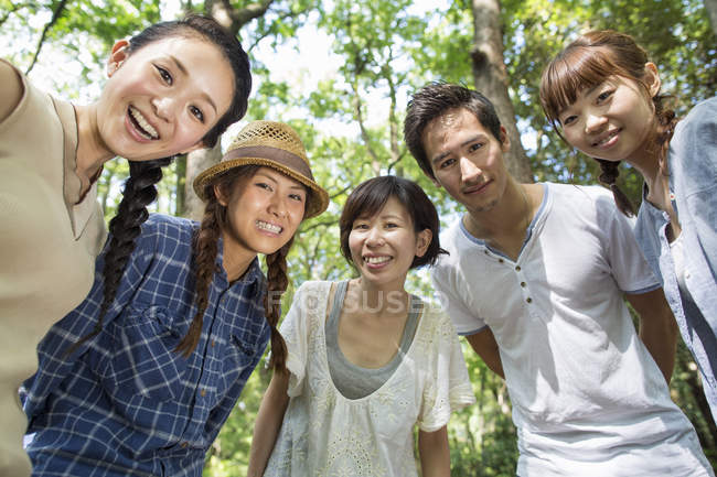 Vista ad angolo basso di amici giapponesi che posano e abbracciano nella foresta . — Foto stock
