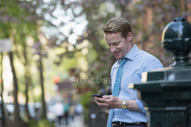 Hombre con camisa y corbata mirando hacia abajo y comprobando el teléfono . - foto de stock