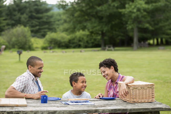 Familie sitzt mit Tellern auf Picknicktisch im Wald. — Stockfoto