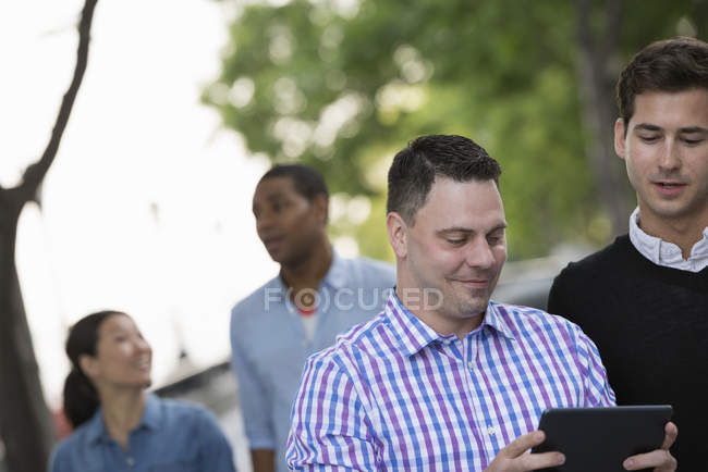 Quatro pessoas na rua e meio homem adulto usando tablet digital . — Fotografia de Stock