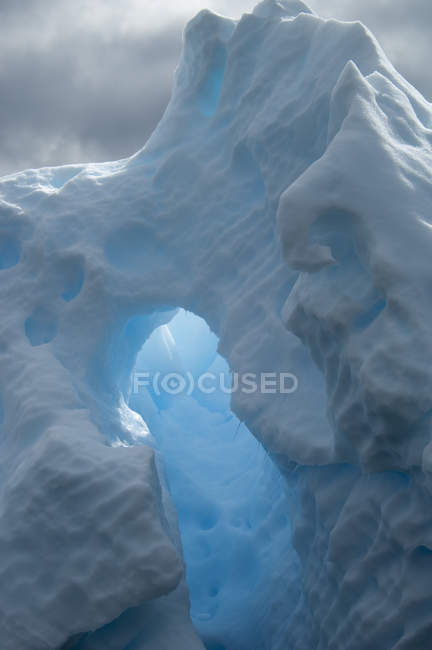 Iceberg with natural arch and translucent glow with sunlight shining through ice. — Stock Photo