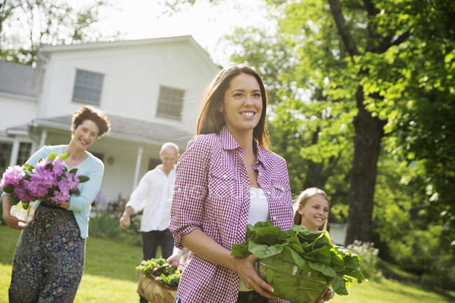 Family walking across lawn carrying flowers, vegetables and fruits. — Stock Photo