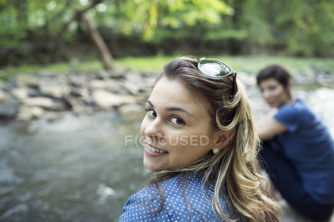 Дві жінки сидять на березі річки і дивляться через плече . — стокове фото