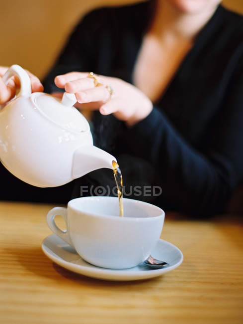Close-up of woman pouring cup of tea from pot at table. — Stock Photo