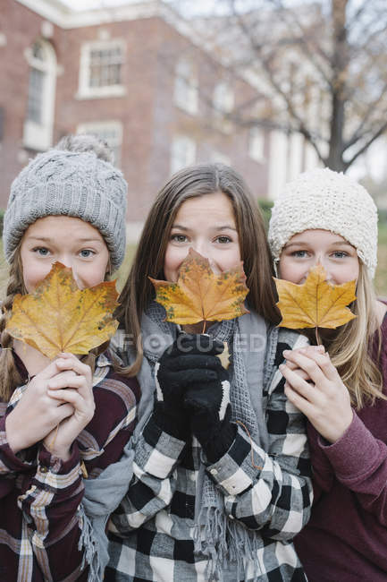 Three teenage girls holding autumnal leaves in front of faces. — Stock Photo