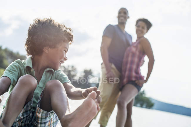 Elementary age boy playing on sunny lake jetty with parents. — Stock Photo