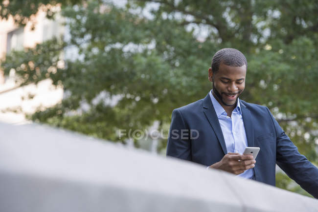 Businessman in blue jacket using smartphone on city park. — Stock Photo