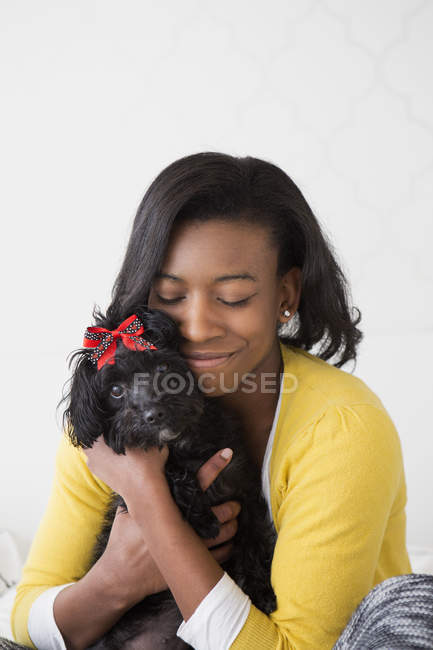 Adolescente menina abraçando pequeno cão de estimação preto com arco vermelho . — Fotografia de Stock