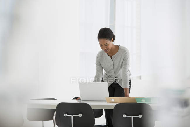 Frau lehnt sich über Schreibtisch und benutzt Laptop im Büro. — Stockfoto