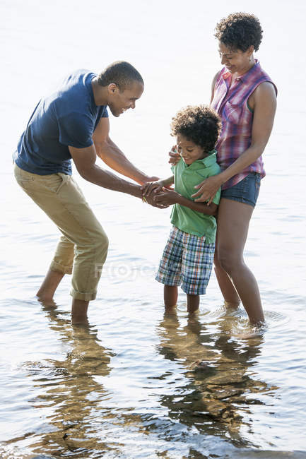 Family with son standing in water on shore of lake. — Stock Photo