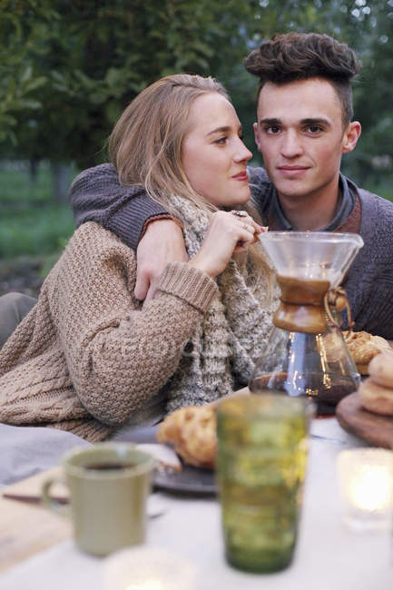 Casal abraçando enquanto sentado na mesa ao ar livre com comida e bebida . — Fotografia de Stock